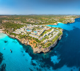 Naklejka premium Aerial drone panorama view of sea coast with white resort houses on rocky cliffs. Turquoise blue sea water, sunny sky, boats, sandy beach. Luxury travel destination, Mallorca island, Spain. Top view