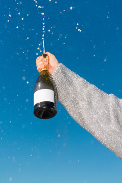 Hand spraying champagne bottle with blank label outdoors