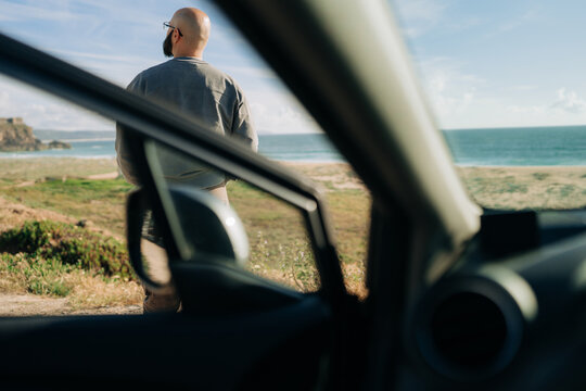 Rear View of Man Looking at Ocean Framed by Car Door