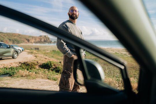 Man Standing Near Coast Viewed Through Open Car Door