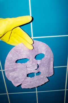 Yellow glove hand holding a beauty product smiley facemask with flash
