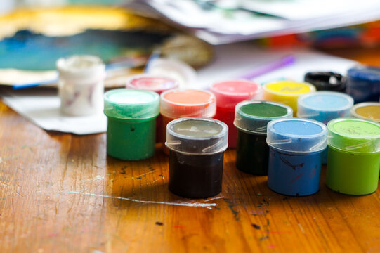 Colorful gouache paint jars on an artist desktop with sketches in the background