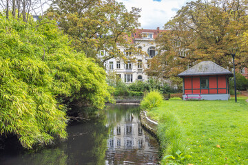 Naklejka premium Ghent town in Belgium, Europe. Tranquil Urban Waterway with Historic Architecture and Lush Greenery Reflect in Calm Waters on an Overcast Day