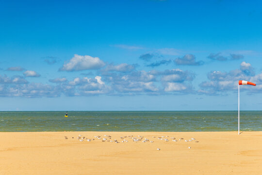 Vibrant Beach Scene on a Sunny Day with Turquoise sea, Golden Sand, Fluffy Clouds, and a Red-White Wind Indicator. Ostend, a coastal city in Belgium, Europe.