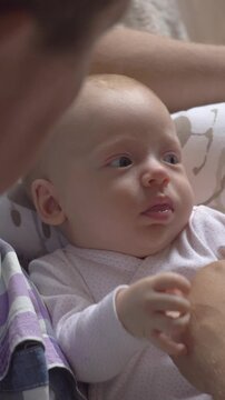 Vertical footage of grandpa babysitting two months old baby granddaughter. He holding child on the lap, looking at her and touching little hands