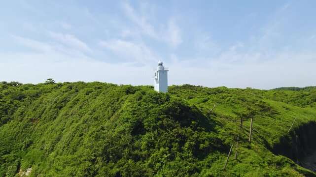 松の森に立つ加佐の岬灯台 ドローン至近距離空撮 左旋回 / Aerial drone orbiting left close-up of Cape Kasa Lighthouse surrounded by lush green forest, Ishikawa
