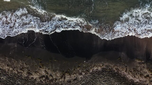 Waves roll towards the shore as the tide rises, creating a line of foam on the sandy beach. The sunlight reflects off the water, highlighting the movement of the ocean.