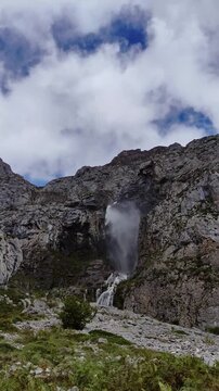 Waterfall that springs from the high mountain on a stormy day covered with clouds and fast gusts of wind.