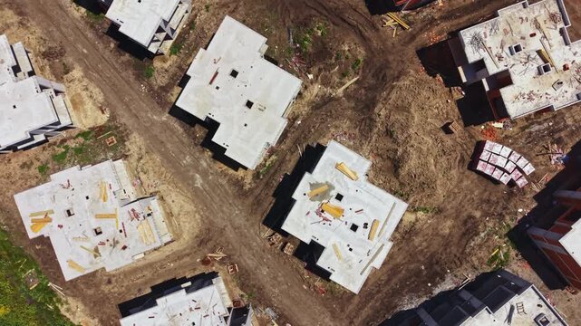 Workers are busy building several houses on a construction site. Roads intersect among the structures with materials scattered around. This scene takes place in a new neighborhood.
