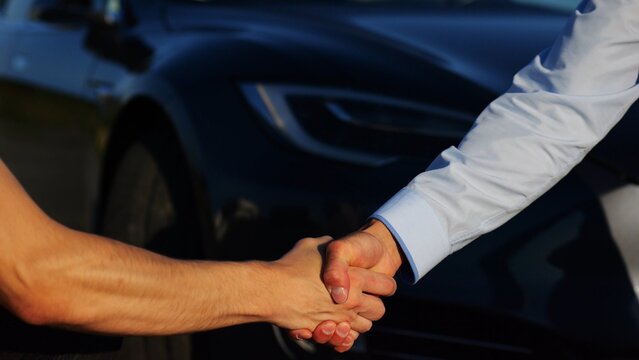 Male hand giving key of car to buyer of electric automobile outdoor. Handshake between salesman and new owner of modern auto after successful deal. Concept of buy or rent car. Slow mo