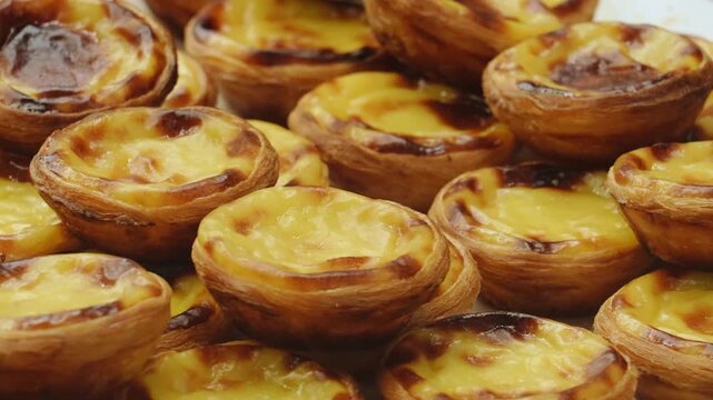 Detailed close-up shot showcasing a pile of freshly baked traditional Portuguese custard tarts with golden, caramelized tops and crispy puff pastry crusts. 