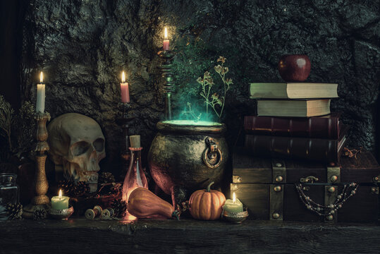 Halloween background. Dark witch cauldron with a magic witch's potion, books, chest, skull. Witchcraft paraphernalia and accessories among candles on a table in a room or cave with stone walls.