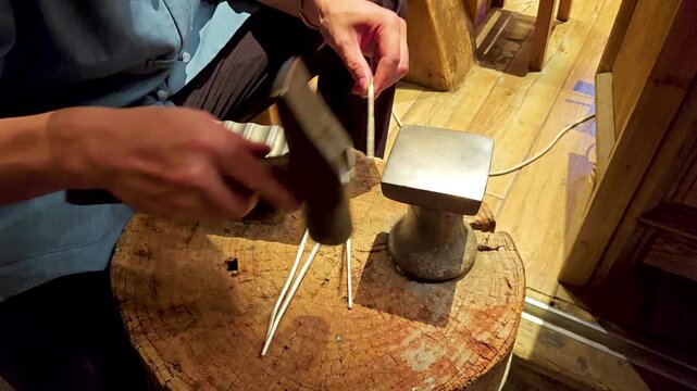 Artisan shaping metal rods by hand on anvil in workshop