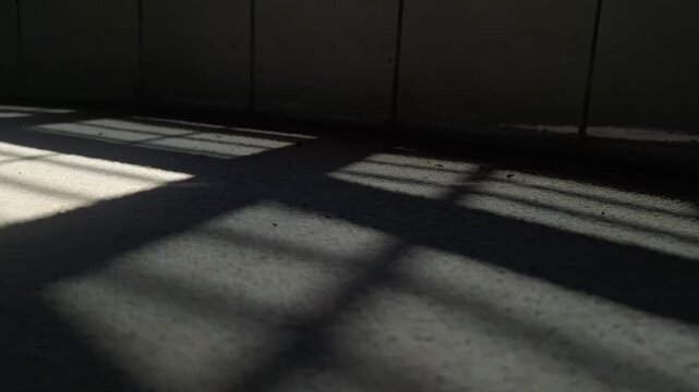Sunlight streaming through window bars casting shadows on a concrete floor