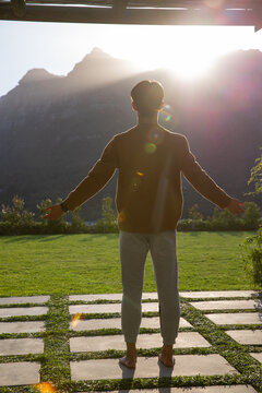 Silhouetted figure standing on grid-style pavers with grass strips and lens flare, facing mountains