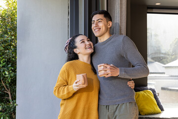Naklejka premium Couple standing in doorway leaning together holding ceramic mugs by sofa and sliding glass door