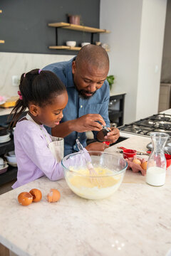 African American father and daughter making batter on marble island, cracking eggs and whisking