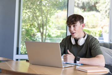Fototapeta premium Youth male speaking and gesturing at table in olive T-shirt with laptop headset watch, copy space