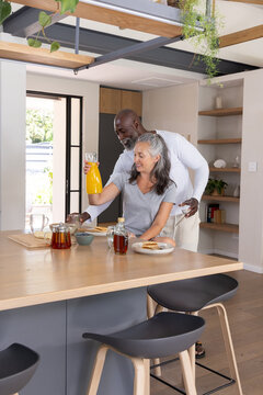 Senior couple preparing breakfast at kitchen island, pouring orange juice and serving toast