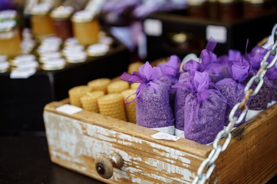 Rustic wooden box filled with dried lavender sachets and honeycomb candles at an outdoor market. Handmade organic crafts, provence style wellness gifts, eco-friendly summer fair concept
