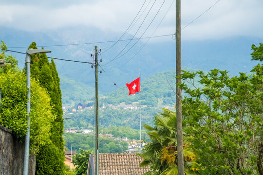 Swiss flag over rooftops with mountain background in Caslano Ticino Switzerland