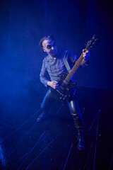 Fototapeta premium Young male rock musician playing electric guitar on dark stage with blue lighting