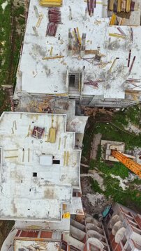 Workers are engaged in building a multi-storey structure with various construction materials visible on the rooftop. Equipment is scattered across the site during the daytime.