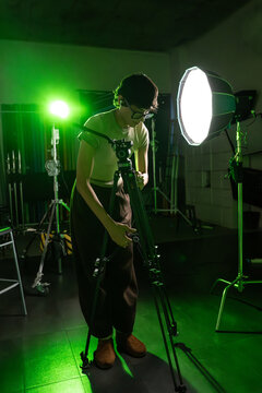 Photographer adjusting tripod camera in studio lighting setup