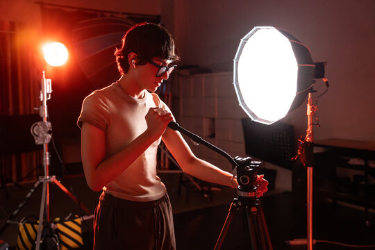 Photographer adjusting video tripod under studio light