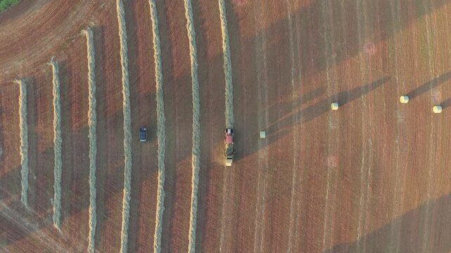 Top-down view of a tractor baling hay and dropping a fresh round bale in a field at sunset