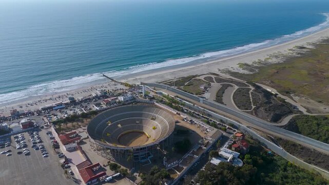 Aerial Flight Over Monumental Bullring and Coastal Border Wall Infrastructure in Tijuana Mexico. The video sequence beautifully centers the massive circular structure of the Monumental Bullring.