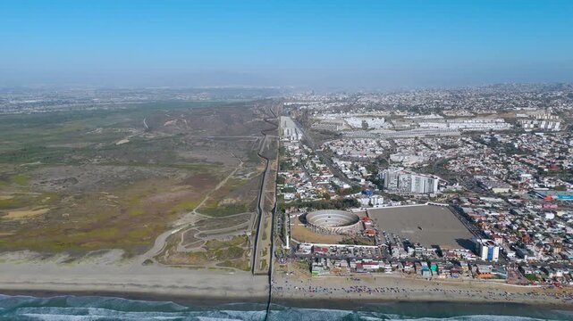 Aerial Establishing Shot of Coastal Landscape and Border Wall at Playas de Tijuana Mexico. The video captures the international border wall infrastructure slicing across the sandy public beach.