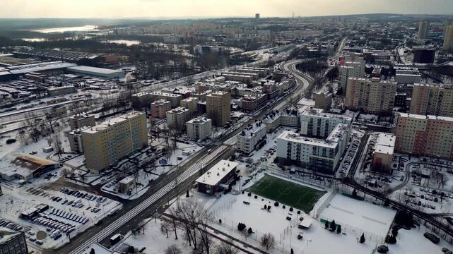 Aerial view of a winter cityscape with a green sports field and residential apartment blocks covered in snow, Katowice, Poland.