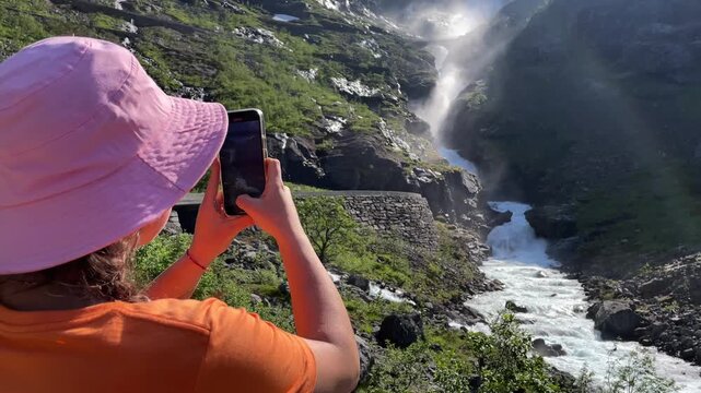 Girl in a bucket hat filming a waterfall with her smartphone