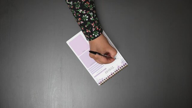 Top Down View of Woman Writing Shopping List in Planner Notebook