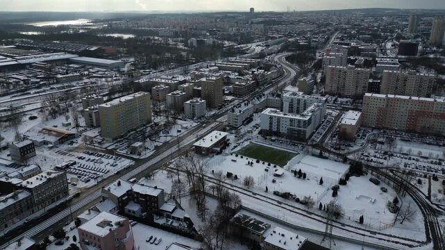 Aerial wide view of a winter cityscape with a green football field, residential blocks and snow covered streets, Katowice, Poland.