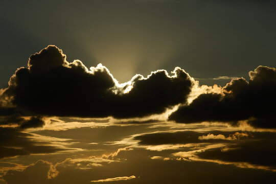  massive dark clouds dramatically backlit by intense golden sunlight breaking through the cloud cover. Spectacular crepuscular rays radiate Super El Ni&ntilde;o climate phenomenon and global warming.