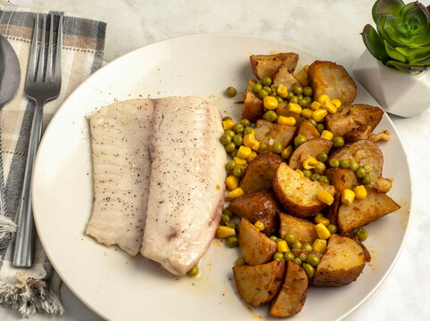 baked cod   with potato wedges , peas and corn