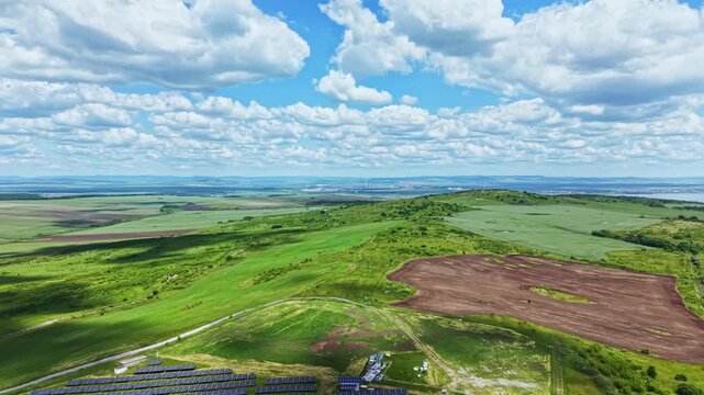Aerial view green hill farmland cleared patch under dramatic clouds, drone mapping for potential solar development, rolling terrain, vivid vegetation, planning