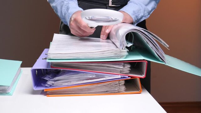 Person inspecting stacks of binders and documents with a magnifying glass, conducting a meticulous financial audit or legal review of records, receipts and accounting files at a desk