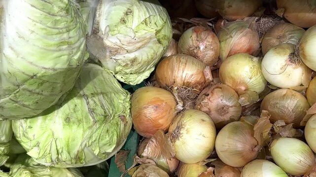 Fresh green cabbage and yellow onions stacked in a market display with visible textures