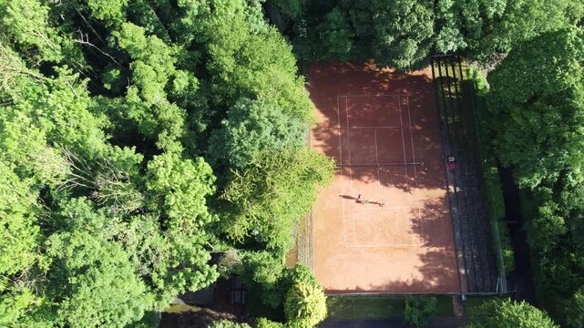 a clay tennis court from a bird's-eye view, surrounded by dense greenery.