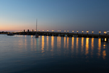 Obraz premium Sunrise and Sunset Over Historic St. Augustine, Florida. Castillo de San Marcos Silhouette with Palm Trees, Sailboats, and Bridge of Lions Reflecting on Matanzas Bay