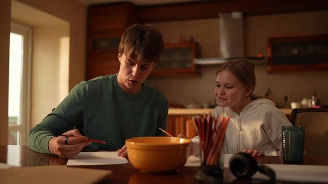 A child learns to draw with help from an adult in a kitchen while enjoying time together in the afternoon