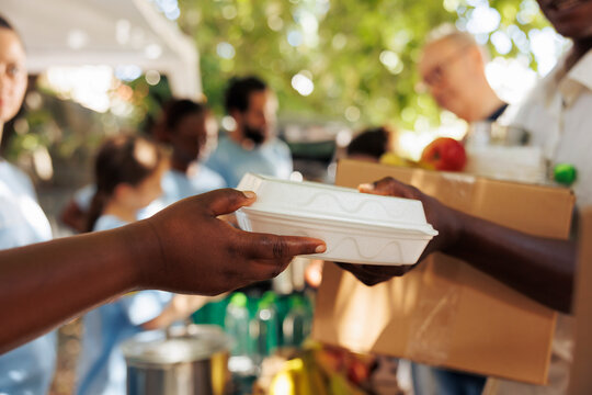 Volunteer of african american descent offers warm meal to an impoverished and hungry individual. Photo focus on the less fortunate person receiving complimentary food from charitable worker.