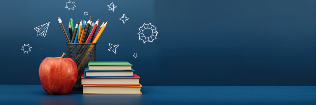 Back to school concept with red apple stacked books and pencils in holder against a dark blue chalkboard wall