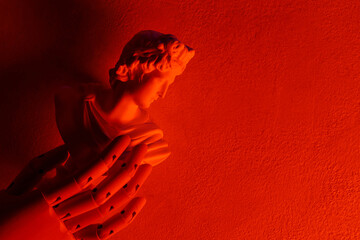 Obraz premium Classical angel statue with praying hands illuminated by dramatic red lighting on textured wall
