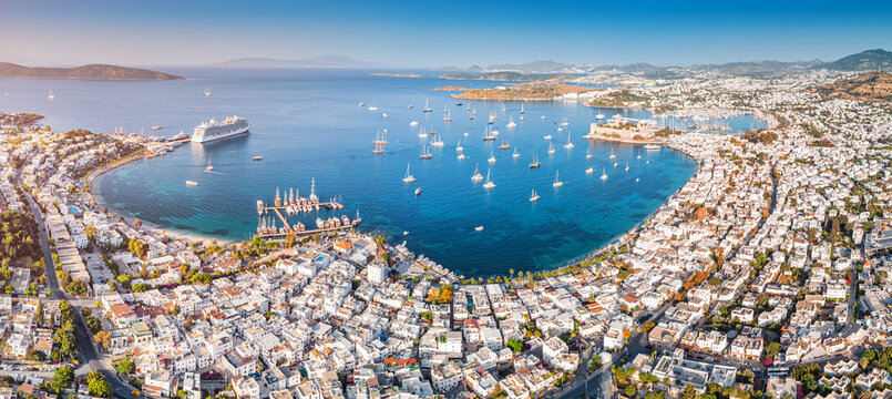 Aerial view of Bodrum, Turkiye coastline featuring a bustling harbor with numerous boats anchored in the clear Aegean Sea, overlooked by castle