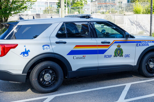 A white RCMP police Ford Explorer SUV with the force rainbow stripe livery, mountie crest and Canada wordmark, parked in a downtown lot.