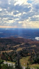Obraz premium Breathtaking mountain view of autumn forest valley with sun rays breaking through dramatic clouds